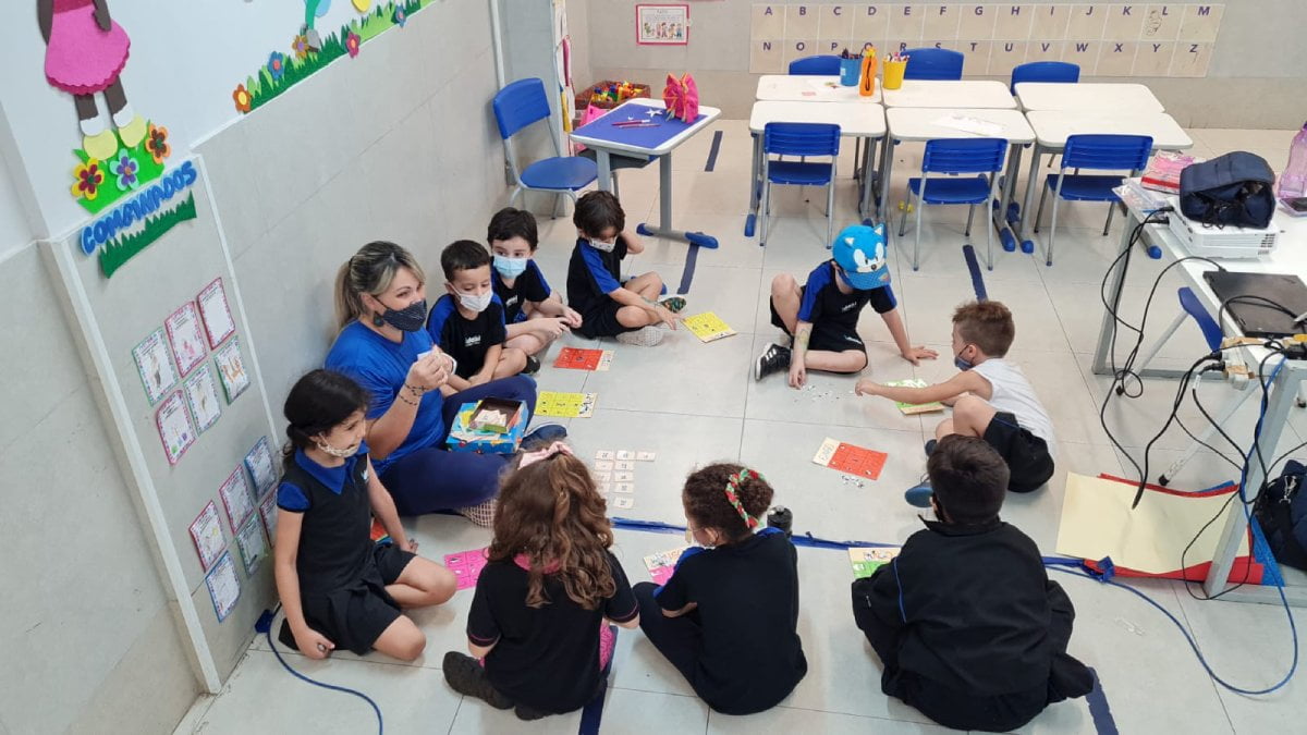 Crianças em sala de aula sentadas em formato de roda, no chão com a professora