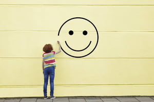 Criança desenhando rosto sorrindo em muro amarelo