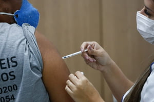 Imagem de uma pessoa aplicando a vacina da gripe no braço de uma pessoa morena de costas 0 Metrópoles