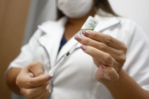 imagem colorida mostra mulher usando jaleco branco e máscara segurando seringa e vidro de vacina da gripe - Metrópoles