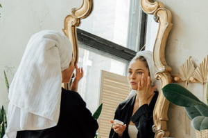 Jovem mulher com toalha na cabeça se olhando no espelho - Metrópoles