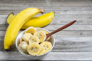 Foto colorida de duas bananas e da fruta cortada em uma tigela - Metrópoles