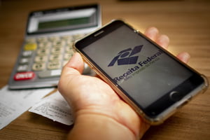 Imagem colorida de um celular com o símbolo da Receita Federal Imposto de Renda - Metrópoles