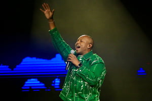 Foto colorida de Thiaguinho cantando no palco vestindo uma roupa verde - Metrópoles