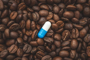 Foto mostra comprimido de suplemnento de cafeína sobre grãos de café - Metrópoles