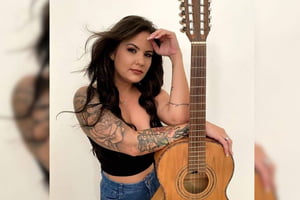 Imagem colorida mostra a cantora sertaneja Nanda Ferraz, uma mulher branca, de cabelos castanho escuros, apoiada em um violão - Metrópoles
