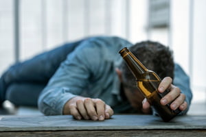 Imagem colorida de homem caído no chão segurando uma garrafa de cerveja - Metrópoles