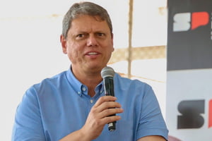Imagem colorida mostra Tarcísio de Freitas, do peito para cima, falando ao microfone. Ele é um homem branco de cabelo grisalho e veste camisa azul clara de manga curta