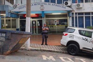 Imagem de policial parado de braços cruzados em frente a entrada de edifício - Metrópoles