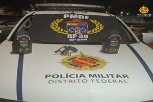 Foto colorida de uma arma de fogo de tambor e munições, colocada em cima do capô de uma viatura caracterizada com o emblema da polícia militar do distrito federal