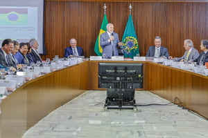 Imagem colorida do presidente Lula de pé com microfone. Ministros estão sentados na mesa ao redor - Metrópoles