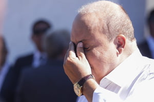 Foto colorida de homem careca com mão ao rosto em expressão de pesar