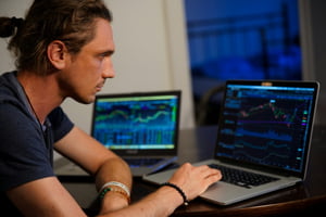 Fotografia colorida de homem com cabelo preso mexendo no mercado de ações pelo computador-Metrópoles