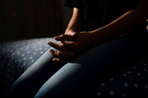Imagem mostra corpo de menina jovem no escuro com as mãos entrelaçadas - Metrópoles