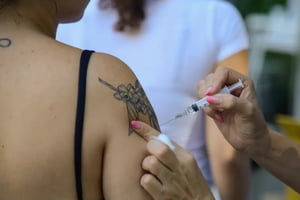 foto colorida de mulher tatuada (pessoa é vista de costas) sendo vacinada contra a gripe - Metrópoles