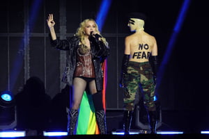 Foto colorida de Madonna cantando no palco com uma bandeira LGBTQIA+
