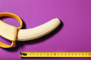 foto colorida de uma banana meio descascada em um fundo roxo com uma fita métrica amarela embaixo - Metrópoles