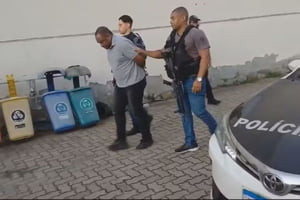 Homem sendo levado por dois policiais com a cabeça abaixada