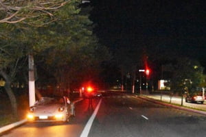 Carro branco estacionado em avenida, à noite - Metrópoles