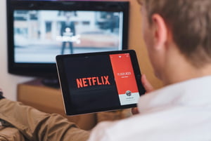 Fotografia colorida mostrando homem sentado em sofá com tablet nas pernas vendo Netflix-Metrópoles
