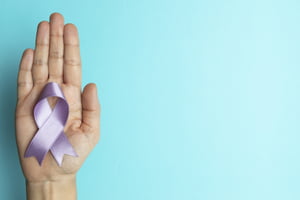 Foto de uma mão segurando uma fita lilás para representar o cuidado aos pacientes com lúpus - Metrópoles