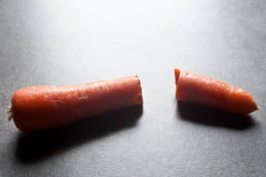Foto colorida de uma cenoura cortada ao meio em uma superfície cinza - Metrópoles