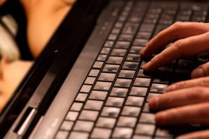 Foto colorida de duas mãos digitando no teclado de um notebook preto - metrópoles