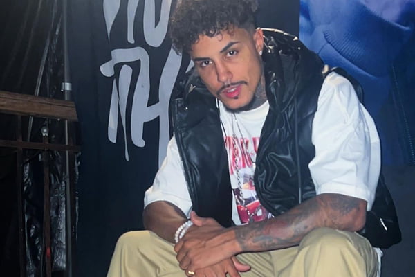 MC Livinho posa de camiseta branca, colete preto e calça bege - Metrópoles