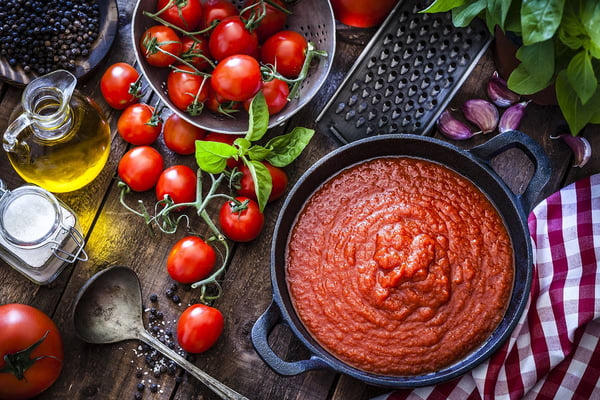 Foto colorida - tomates frescos e uma panela com molho de tomate