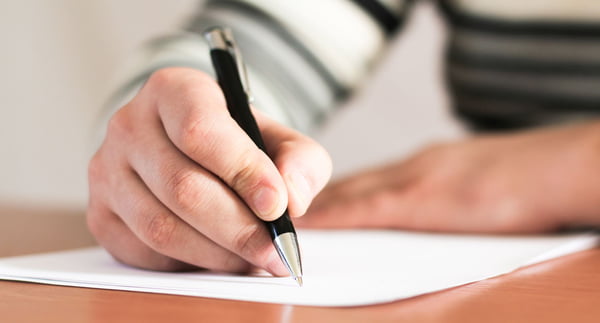 Imagem colorida de pessoa escrevendo com uma caneta em um papel branco - Metrópoles