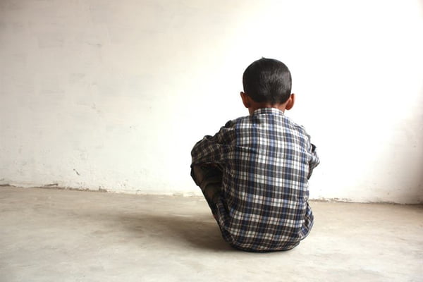 A boy sitting facing a white wall alone