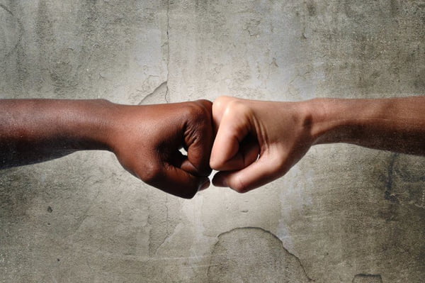 black African American race female hand touching knuckles with white Caucasian woman in multiracial diversity