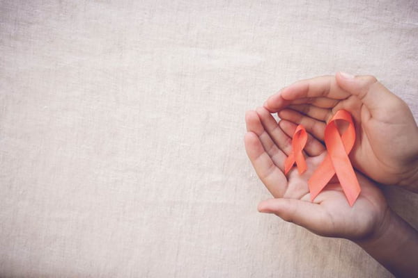Orange Ribbons on hands on toning background, Leukemia awareness
