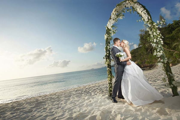 Gorgerous couple kissing, standing under arch during sunset.