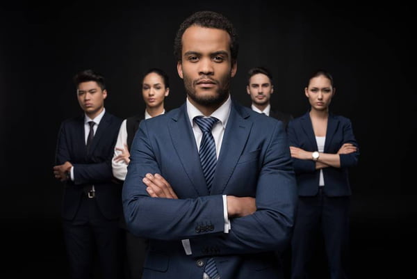 Serious businessman with his business colleagues standing with arms crossed and looking at camera isolated on black