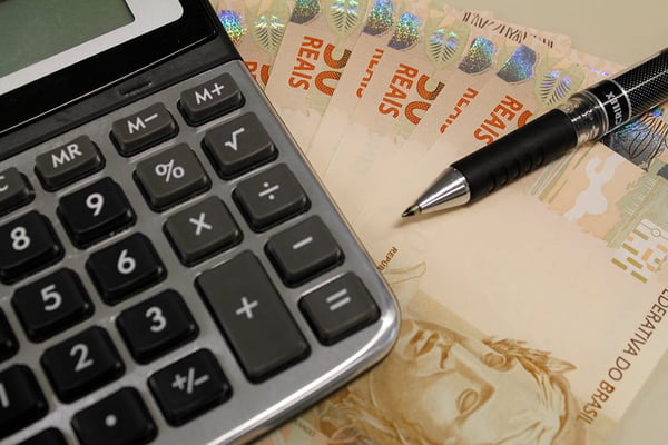 Imagem colorida de uma calculadora e notas de dinheiro - Metrópoles