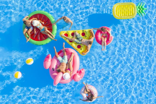 AERIAL: Group of happy attractive people hanging out on fun floaties in the pool