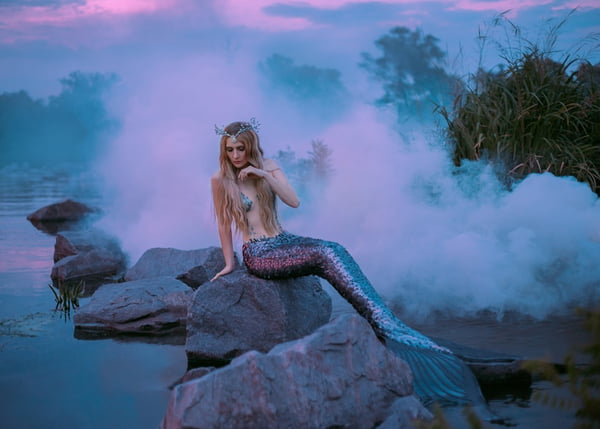 a beautiful mermaid is sitting on the rock in the purple fog