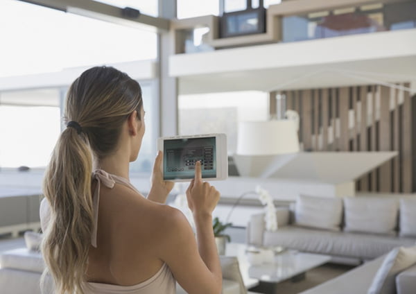 Woman with digital tablet setting digital security system in modern, luxury home showcase interior living room