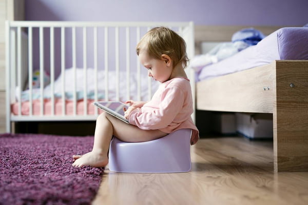 Toddler sitting on potty playing with digital tablet