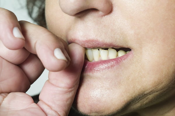 Imagem colorida de boca feminina no ato de roer unhas - Metrópoles