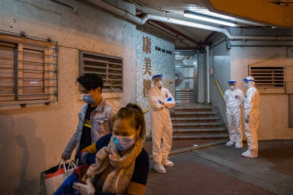 Coronavírus – Funcionários usando equipamentos de proteção ficam do lado de fora do edifício residencial da Hong Mei House