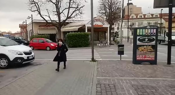 Mulher anda sozinha, com máscara, na rua em cidade italiana