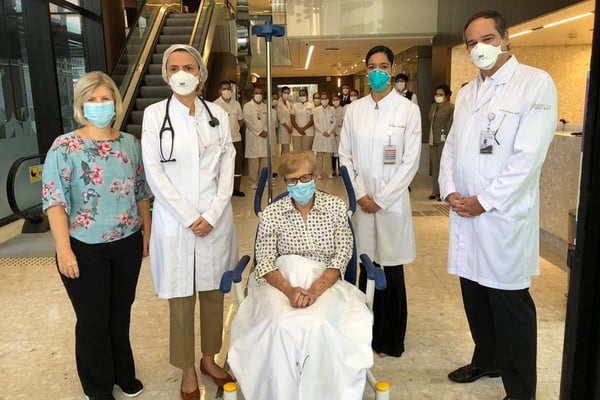 Dona Gina cercada pela equipe do hospital, todos de máscara