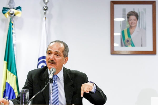 Aldo Rebelo em frente a uma foto de Dilma Rousseff com a faixa presidencial na parede