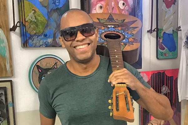 Salgadinho segurando um violão no ombro, usando óculos de sol