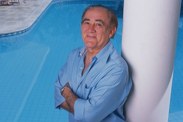 Renato Aragão em frente a uma piscina, de braços cruzados