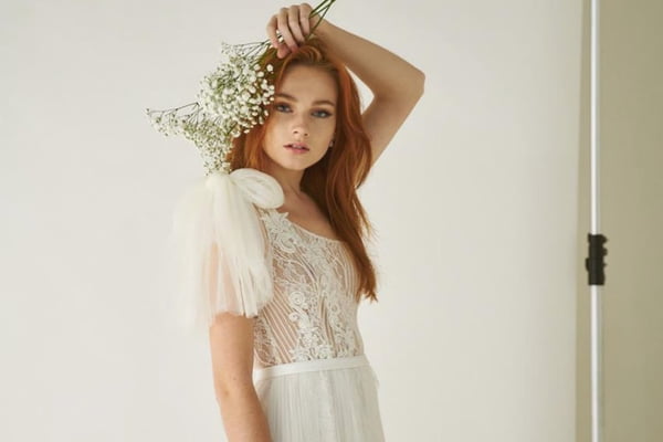 Modelo posa com vestido de noiva e segurando raminho