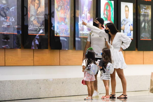 Homem, mulher e duas crianças meninas olhando cartazes de cinma