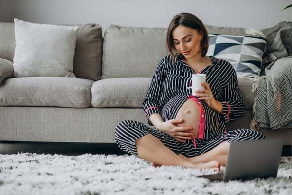 Mulher grávida sentada no chão com xícara na mão
